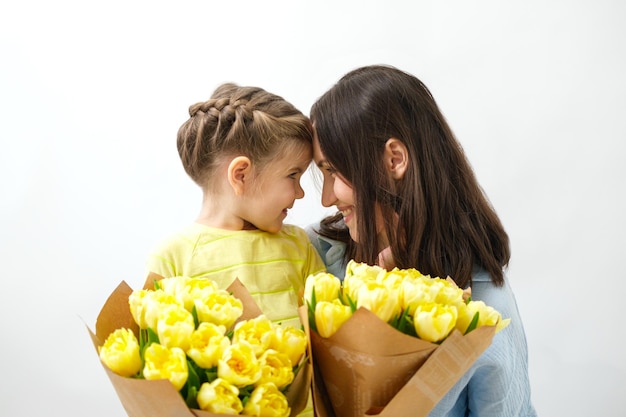 Portrait of smiling mother and daughter with bouquet of yellow tulips looking at each other unconditional love mothers day concept