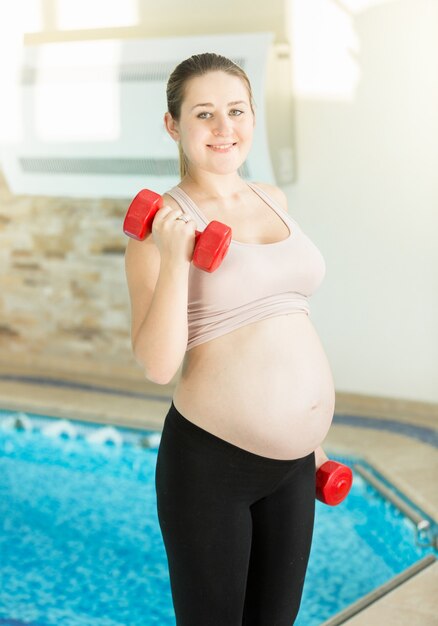 Portrait of smiling pregnant woman lifting up dumbbells at gym