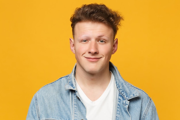 Portrait of smiling pretty young man wearing denim casual clothes looking camera isolated on yellow orange wall background in studio. People sincere emotions, lifestyle concept. Mock up copy space.