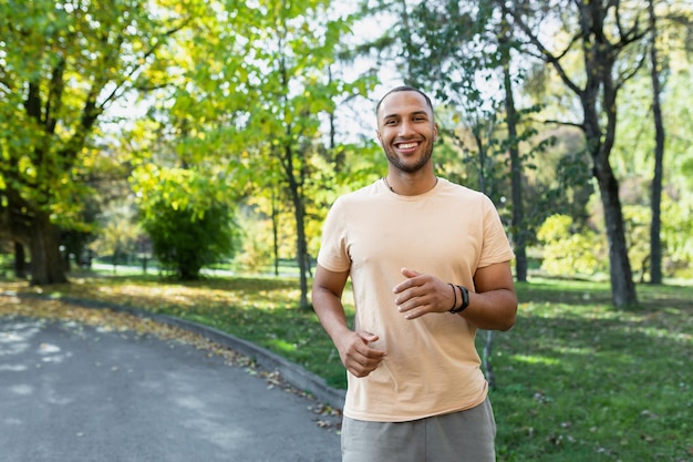 Portrait of smiling and satisfied african american man jogging in sunny park man happy and looking