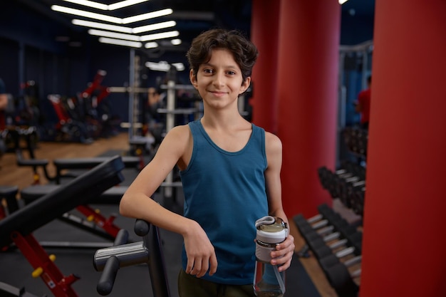 Portrait of smiling satisfied preteen boy drinking water after training