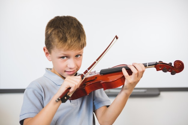 Portrait of smiling schoolboy playing violin in classroom