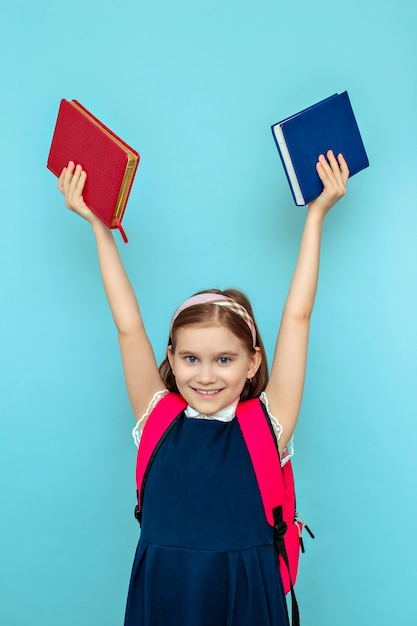 Portrait of a smiling schoolgirl child with a school bag and books, hands raised up