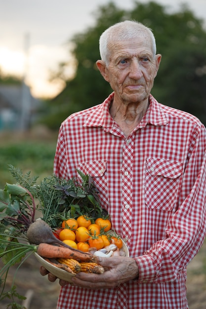 Portrait of smiling senior man in the garden with a bowl of vegetables from your garden