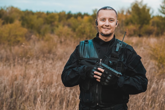 Portrait of smiling special forces soldier in black uniform with a pistol