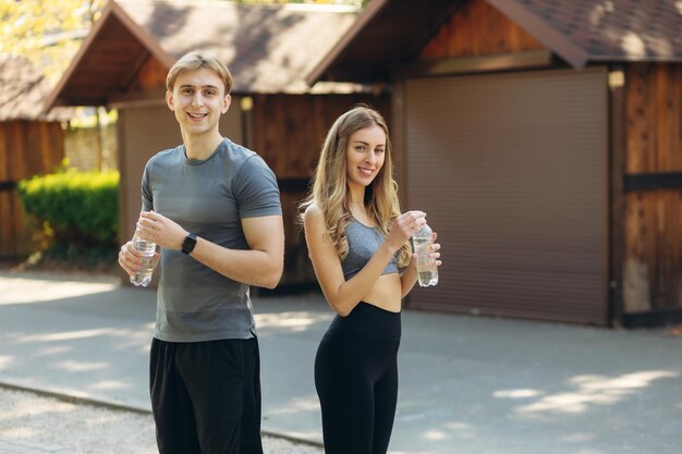 Portrait of smiling sports couple holding water bottles in park