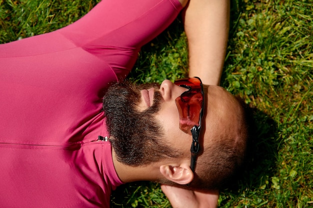 A portrait of a smiling sports man lies on the green grass on a field The concept of fatigue from outdoor training