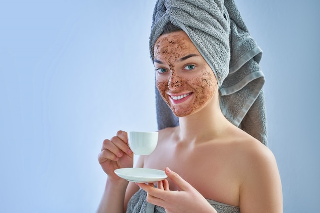 Portrait of smiling woman in bath towel with natural face coffee scrub mask after shower