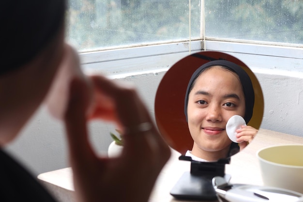 Portrait of smiling woman cleansing face using cotton on the mirror 