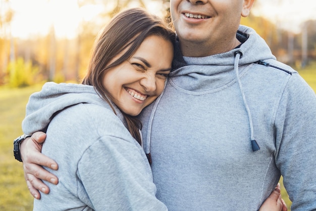 Portrait of a smiling woman enjoying hug of her man and smiling middleaged couple embracing in park ...