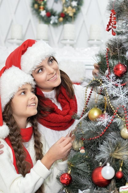 Portrait of smiling woman and girl  decorating Christmas tree together and looking at the camera