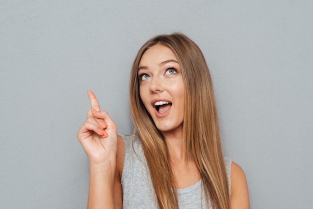 Portrait of a smiling woman pointing finger up at copyspace isolated on a gray background