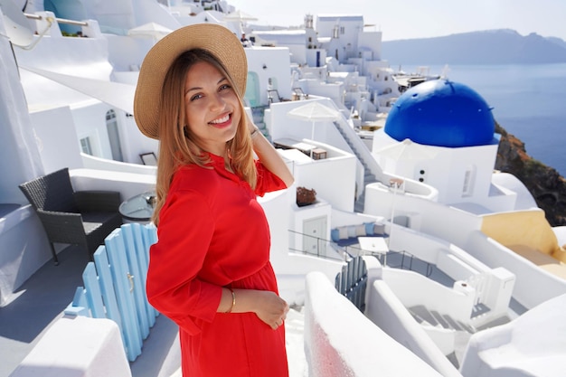 Portrait of smiling woman in red dress turns around and smiling at camera when goes down the steps in Oia village Greece Europe