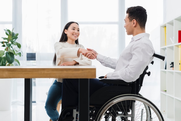 Portrait of a smiling woman shaking hand with disabled young man sitting on wheel chair