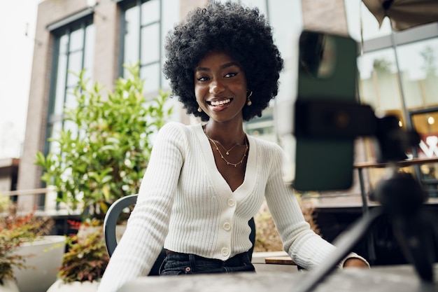 Portrait of smiling woman with afro hairstyle on video call sitting in cafe