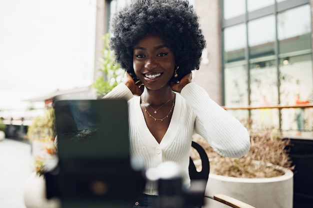 Portrait of smiling woman with afro hairstyle on video call sitting in cafe