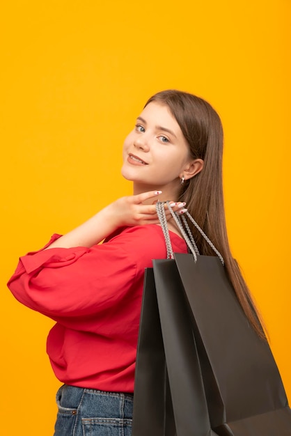 Portrait of smiling woman with big black shopping bags Woman after good shopping Bright yellow background Vertical frame