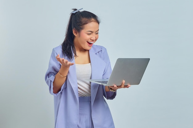 Portrait of smiling young Asian woman looking at laptop and celebrating success of getting new project isolated on white background