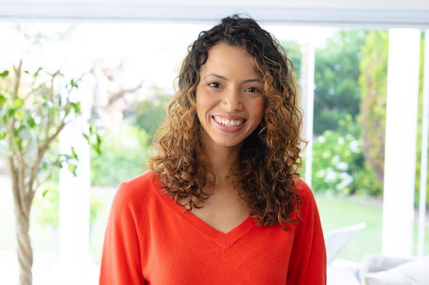 Portrait of smiling young beautiful biracial woman with curly hair standing at home