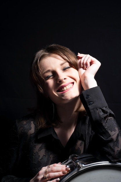 Portrait of a smiling young beautiful drummer girl in black holding a snare drum posing On a black background Dramatic portrait