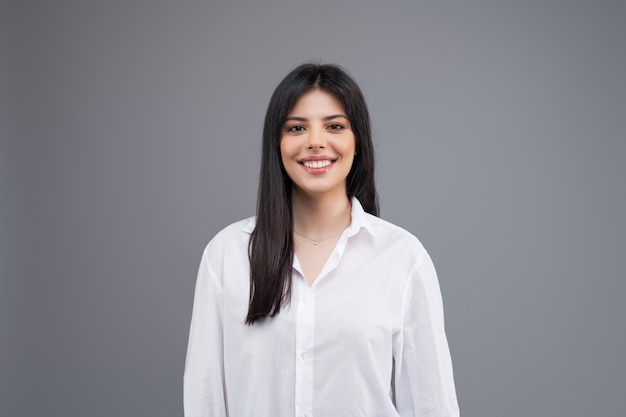 Portrait of a smiling young business woman in white shirt isolated over grey background