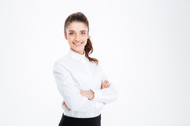 Portrait of a smiling young businesswoman standing with arms folded isolated on a white wall