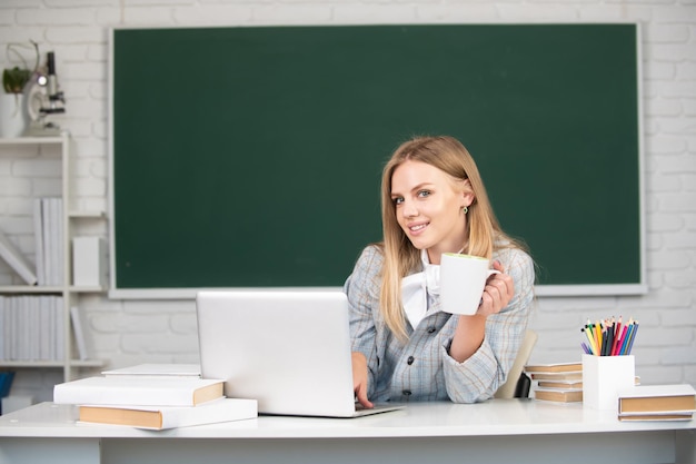 Portrait of smiling young college student drinking coffee or tea studying in classroom