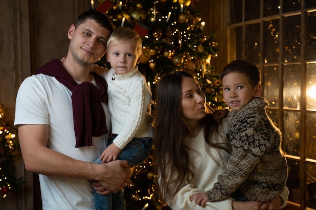 Portrait of a smiling young family with young children near the christmas tree waving a greeting to