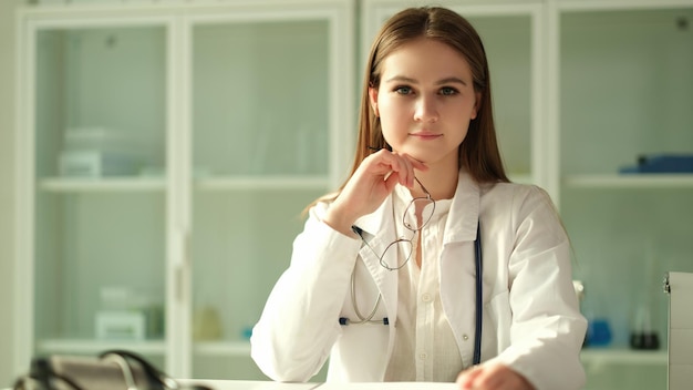 Portrait of smiling young female doctor at workplace holding eyeglasses in clinic