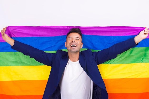 Portrait of a smiling young gay man holding a lgbtqi flag on a white background