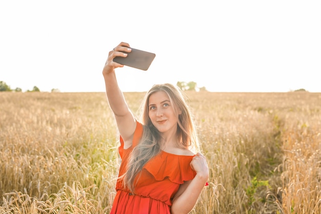 Portrait of a smiling young girl making selfie photo in the field