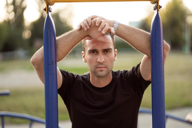 Portrait of a smiling young male athlete leaning on horizontal bars resting after running