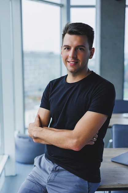 Portrait of a smiling young man in a black tshirt against the background of a modern office Stylish guy in casual clothes