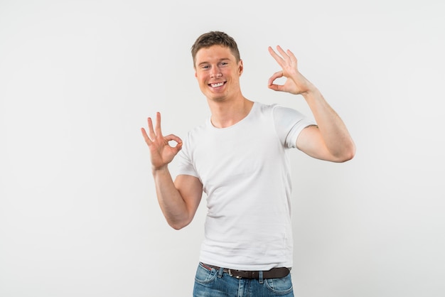 Portrait of a smiling young man showing ok sign against white backdrop