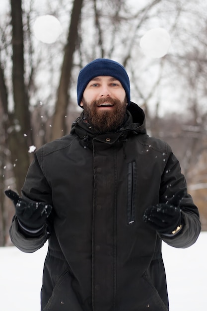 Portrait of a smiling young man wearing hat with a snowball in his hand