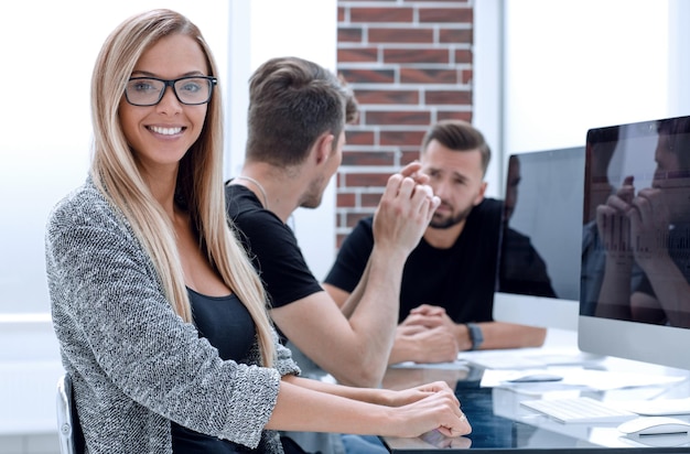 Portrait of a smiling young woman on the background at her colleagues while working on a laptop in the office