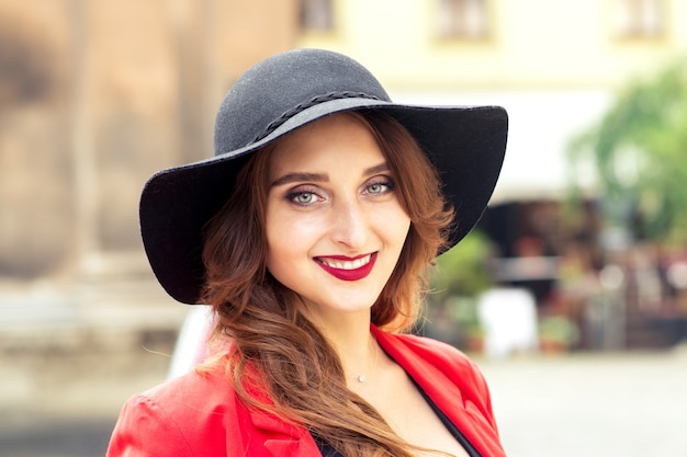 Portrait of smiling young woman in black hat looking at camera outdoors.