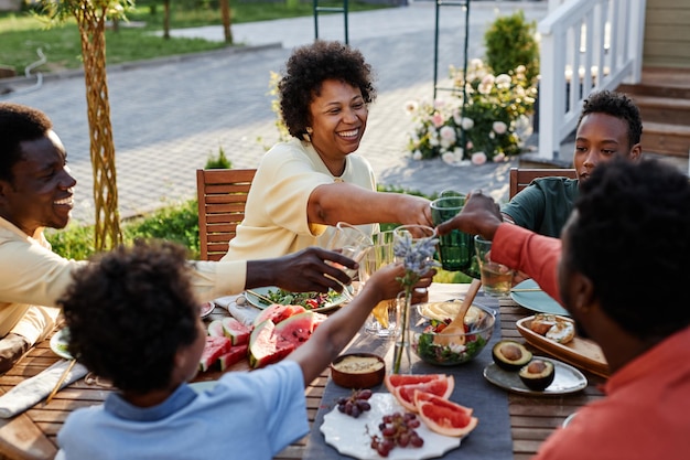 Portrait of smiling young woman clinking glasses with family and friends while enjoying dinner outdo