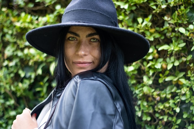 Portrait of a smiling young woman in a hat with green leaves in the background outdoors