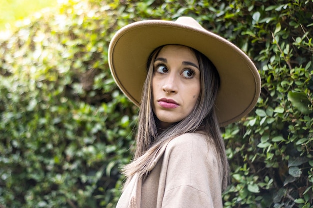 Portrait of a smiling young woman in a hat with green leaves in the background outdoors