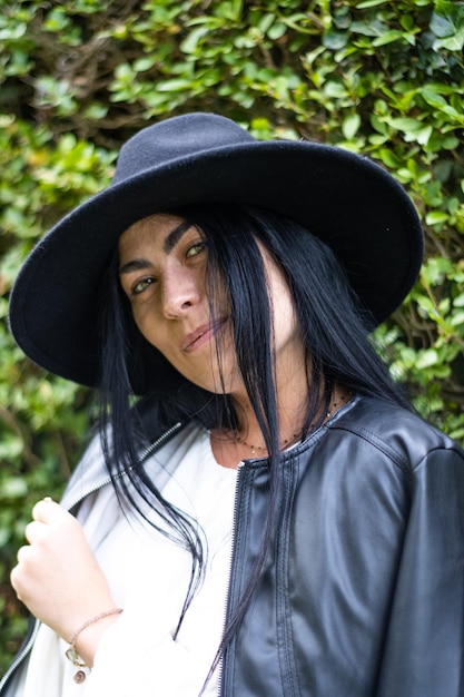 Portrait of a smiling young woman in a hat with green leaves in the background outdoors