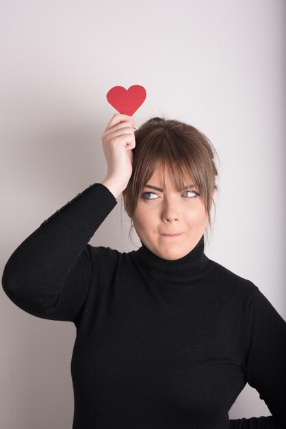 Photo portrait of smiling young woman holding heart shape over white background