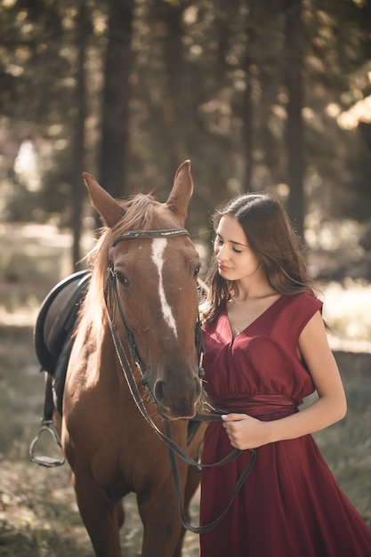 Portrait of a smiling young woman hugging her brown horse. A girl in a dress is standing near a horse. The concept of friendship between people and pets.