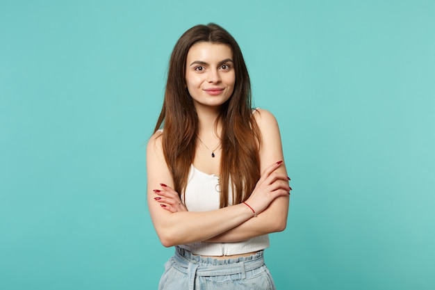 Portrait of smiling young woman in light casual clothes looking camera, holding hands crossed isolated on blue turquoise wall background. People sincere emotions lifestyle concept. Mock up copy space.