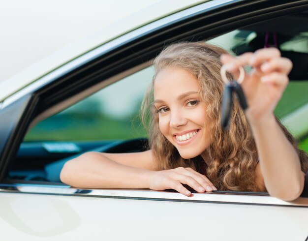 Portrait of Smiling Young Woman Looking out of the Window of her Car Showing Car Key