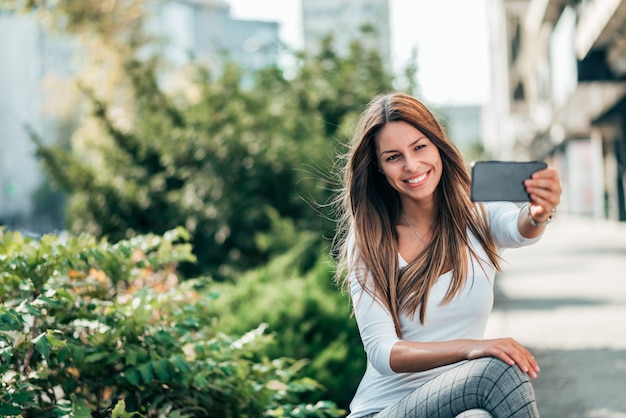 Portrait of smiling young woman making selfie in the town street.