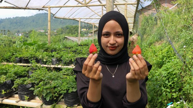 Portrait of smiling young woman picking fresh strawberries at strawberries garden