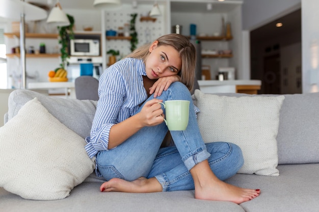 Portrait of a smiling young woman relaxing alone on her living room sofa at home in the afternoon