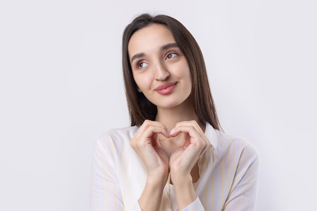 Portrait of a smiling young woman showing heart gesture with her fingers isolated over white background