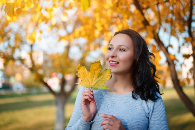 Portrait of smiling young woman with autumn leafs in front of foliage